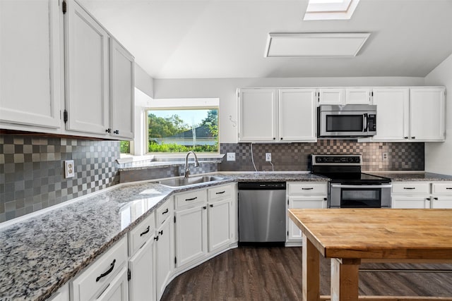 kitchen featuring lofted ceiling with skylight, appliances with stainless steel finishes, light stone counters, and white cabinets