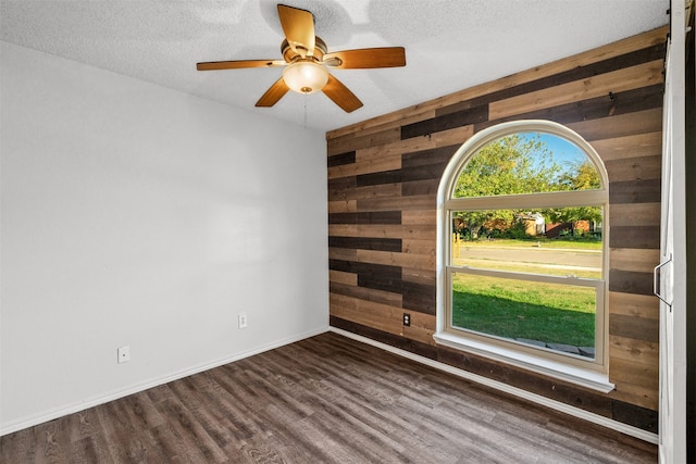 spare room with a textured ceiling, wooden walls, and dark hardwood / wood-style floors