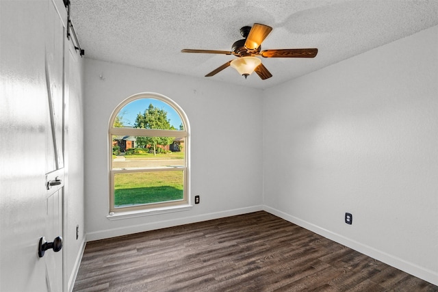 empty room with ceiling fan, a textured ceiling, dark hardwood / wood-style flooring, and a barn door