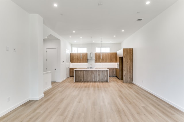 kitchen featuring wall chimney range hood, sink, pendant lighting, light hardwood / wood-style flooring, and a kitchen island with sink