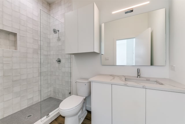 bathroom with toilet, hardwood / wood-style flooring, vanity, and tiled shower