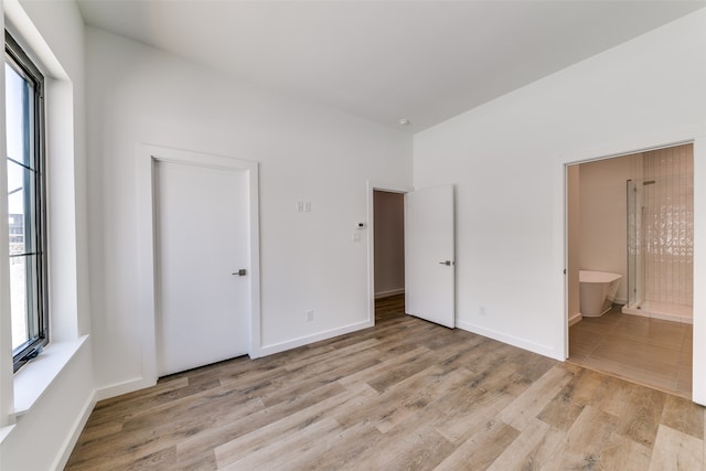 unfurnished bedroom with multiple windows, ensuite bath, and light wood-type flooring