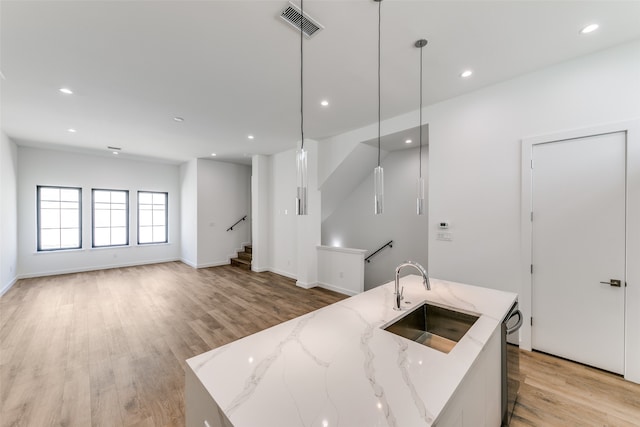 kitchen with light stone countertops, sink, pendant lighting, light hardwood / wood-style flooring, and a center island with sink