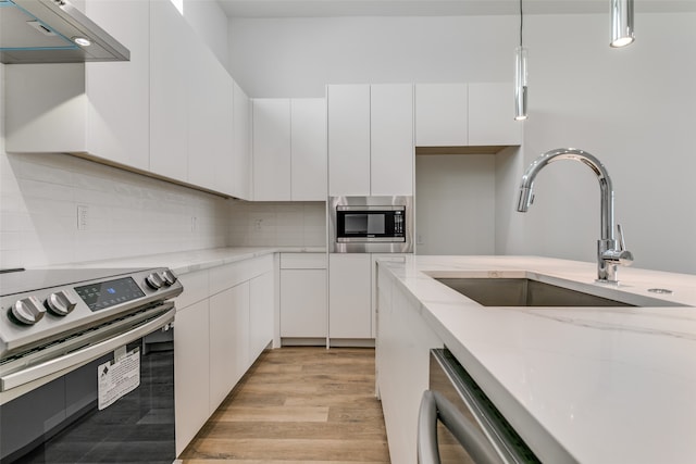 kitchen featuring sink, hanging light fixtures, white cabinetry, stainless steel appliances, and range hood