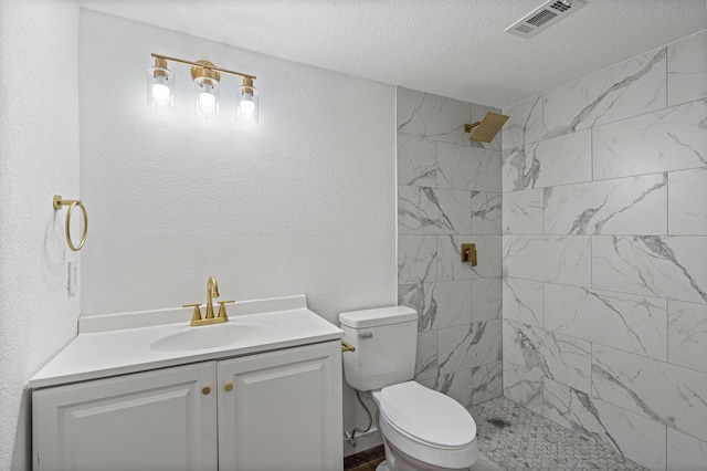 bathroom with vanity, a tile shower, a textured ceiling, and toilet