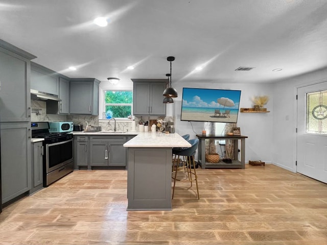 kitchen featuring stainless steel range, a breakfast bar area, gray cabinets, and a wealth of natural light