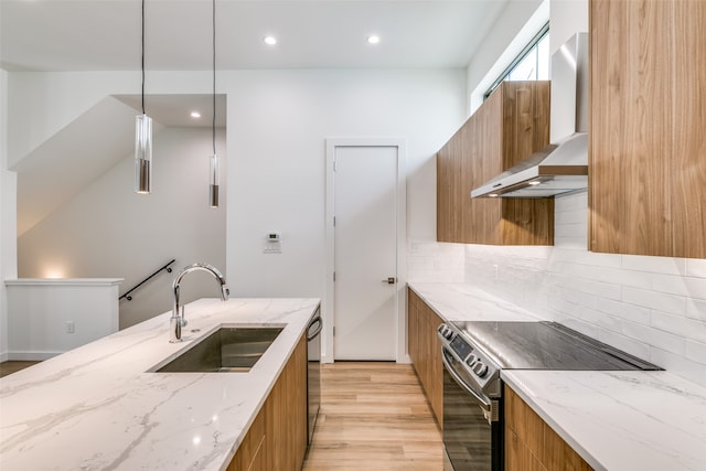 kitchen featuring wall chimney range hood, stainless steel appliances, sink, light stone counters, and light hardwood / wood-style floors