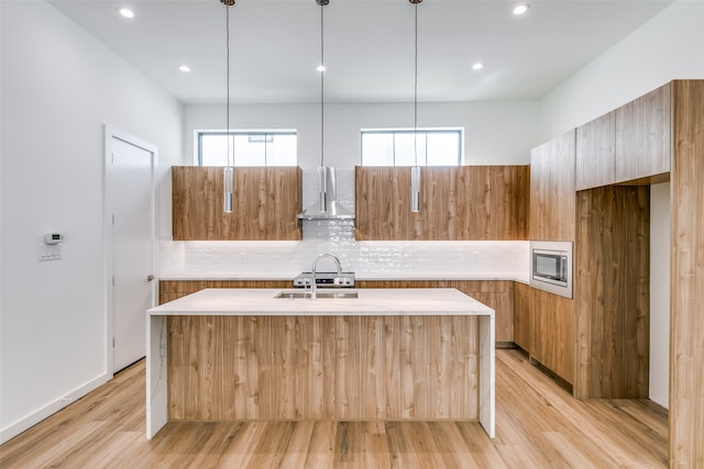 kitchen with a center island with sink, sink, light hardwood / wood-style flooring, and decorative light fixtures