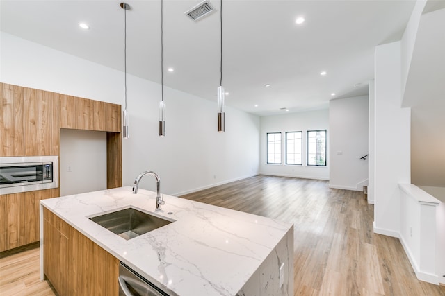 kitchen featuring light hardwood / wood-style floors, sink, decorative light fixtures, and a kitchen island with sink