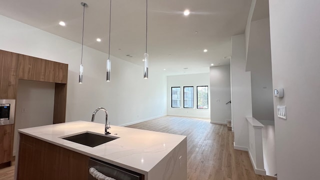 kitchen with sink, an island with sink, hanging light fixtures, light stone counters, and light hardwood / wood-style flooring