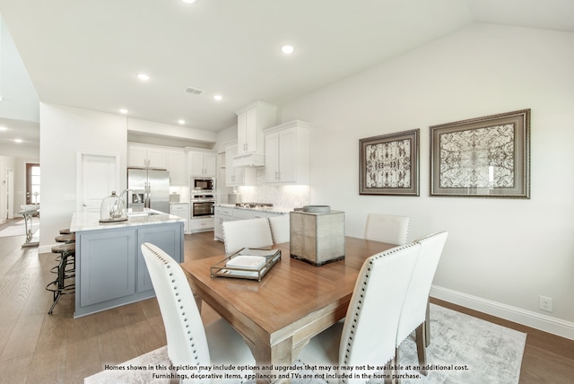 dining area with sink, light hardwood / wood-style floors, and vaulted ceiling