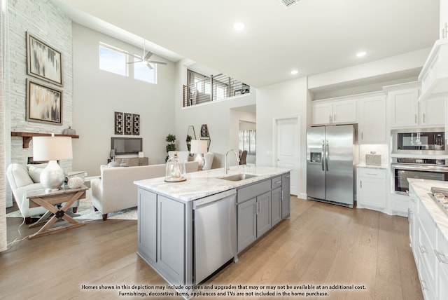 kitchen featuring stainless steel appliances, sink, light wood-type flooring, white cabinets, and a towering ceiling