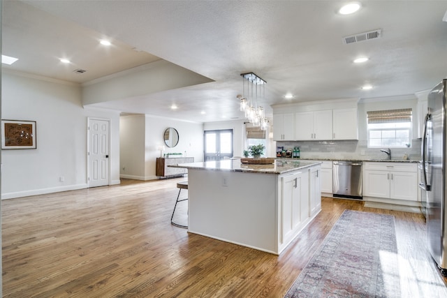 kitchen featuring white cabinets, hanging light fixtures, appliances with stainless steel finishes, light hardwood / wood-style floors, and a center island