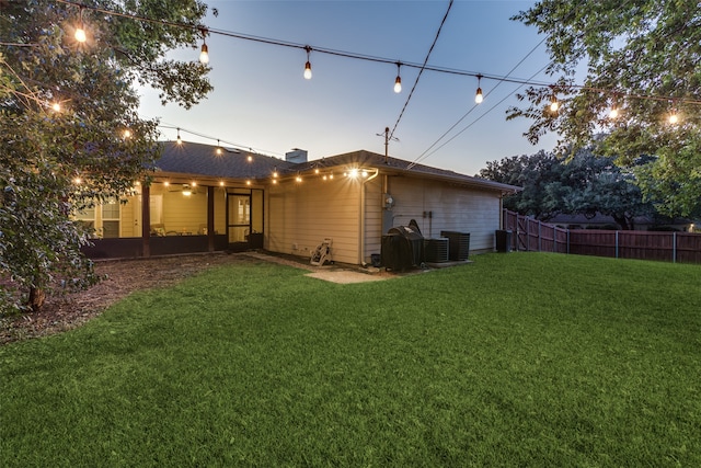 back house at dusk featuring a patio, cooling unit, and a lawn