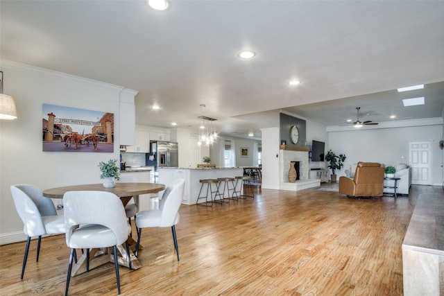 dining area featuring light hardwood / wood-style flooring, ceiling fan with notable chandelier, and crown molding