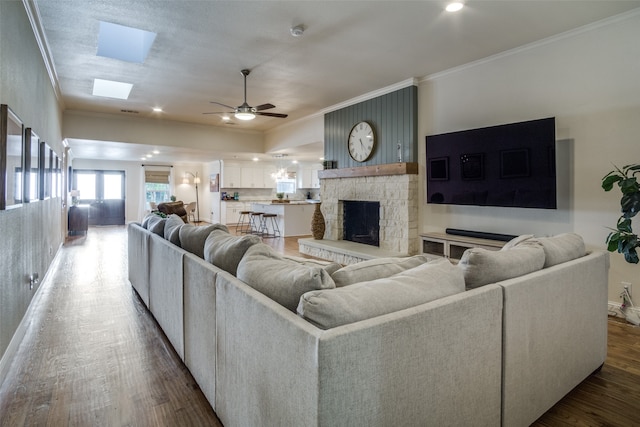 living room featuring ceiling fan, wood-type flooring, a skylight, a fireplace, and crown molding