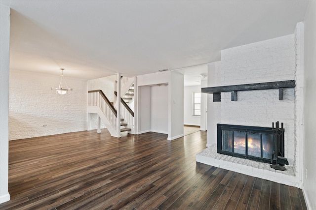 unfurnished living room with a chandelier, dark hardwood / wood-style floors, and a brick fireplace