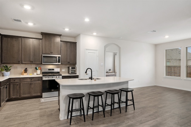 kitchen featuring a center island with sink, appliances with stainless steel finishes, a kitchen bar, light hardwood / wood-style floors, and sink