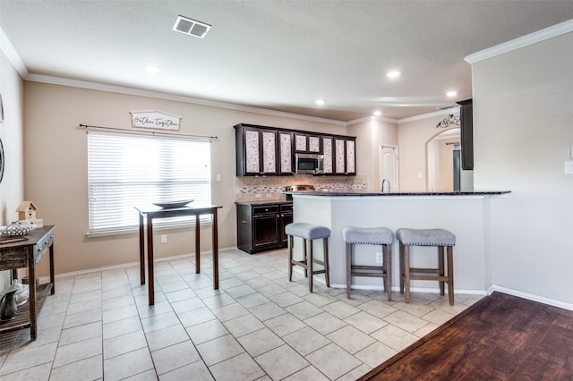 kitchen with stainless steel appliances, ornamental molding, light wood-type flooring, and a kitchen breakfast bar