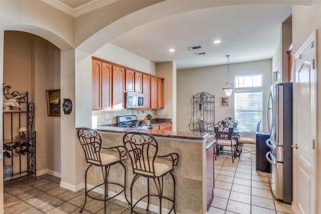 kitchen with backsplash, dark stone counters, ornamental molding, pendant lighting, and stainless steel appliances