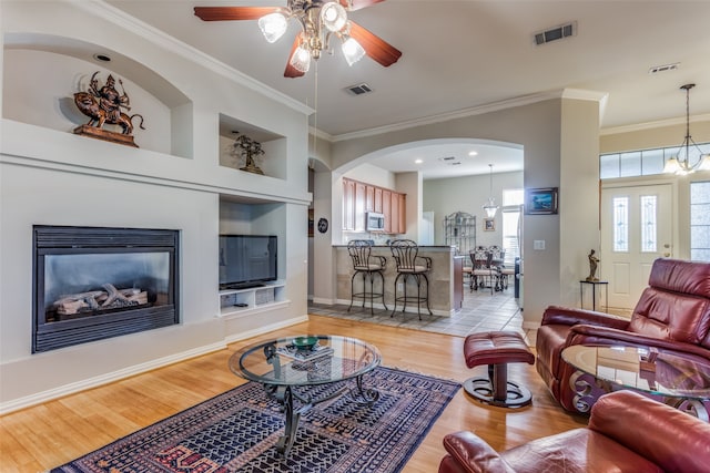 living room with light hardwood / wood-style floors, crown molding, built in features, and ceiling fan