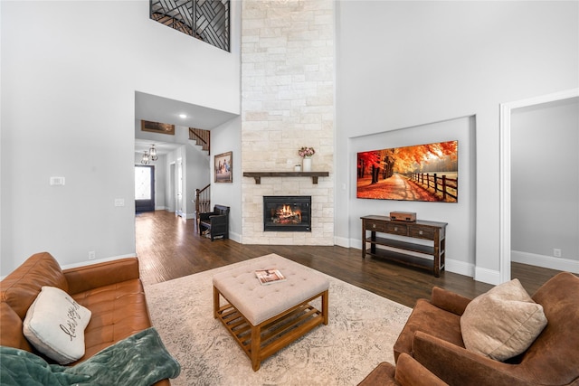 living room featuring an inviting chandelier, a fireplace, dark hardwood / wood-style flooring, and a towering ceiling