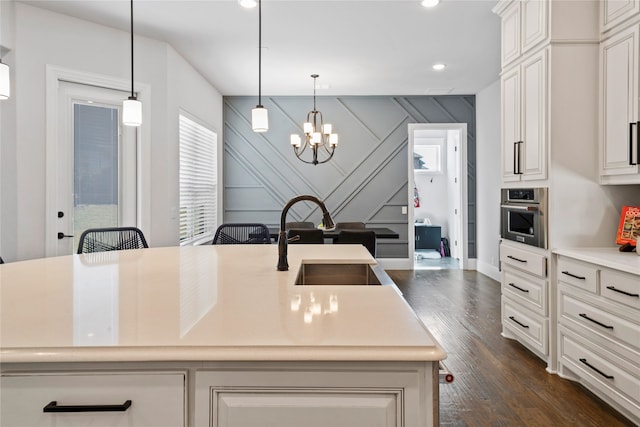 kitchen featuring oven, sink, decorative light fixtures, dark wood-type flooring, and a center island with sink