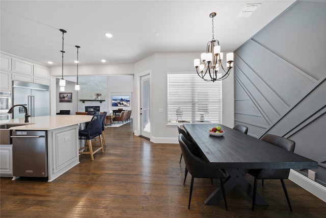 dining area with sink, a stone fireplace, dark hardwood / wood-style floors, and a chandelier