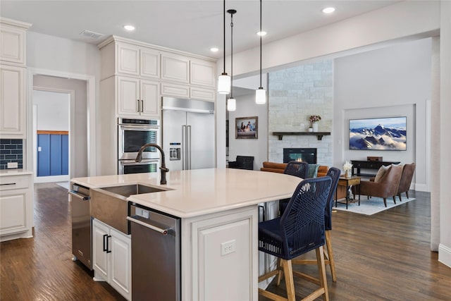 kitchen with pendant lighting, stainless steel appliances, an island with sink, and white cabinets