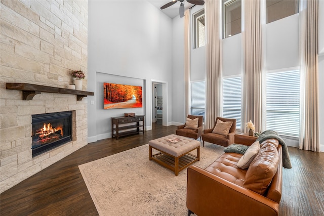 living room with dark hardwood / wood-style floors, ceiling fan, a fireplace, and a high ceiling