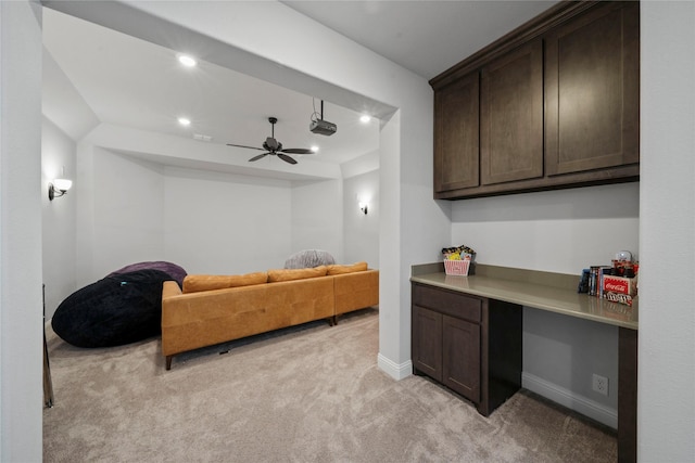 interior space with dark brown cabinetry, ceiling fan, built in desk, and light carpet