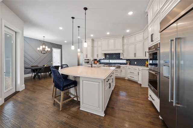 kitchen featuring a kitchen island with sink, hanging light fixtures, dark hardwood / wood-style flooring, and stainless steel appliances