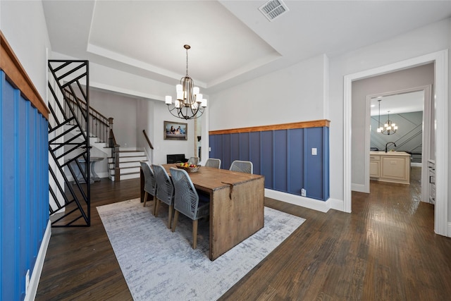 dining space featuring dark wood-type flooring, a chandelier, and a raised ceiling