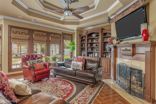 living room featuring ceiling fan, a tray ceiling, a tile fireplace, and ornamental molding