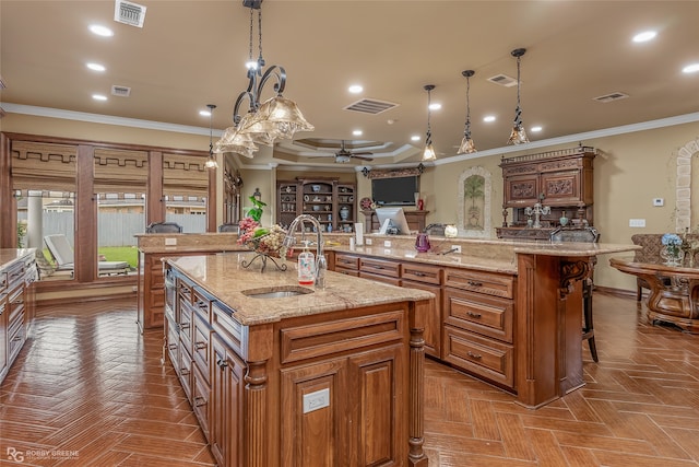 kitchen with light stone counters, a kitchen bar, hanging light fixtures, sink, and a spacious island