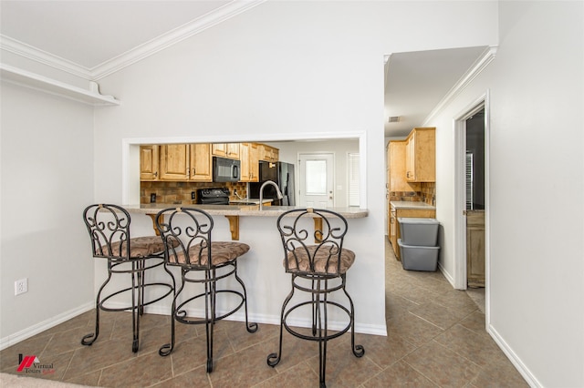 kitchen with light brown cabinets, a breakfast bar area, kitchen peninsula, backsplash, and black appliances