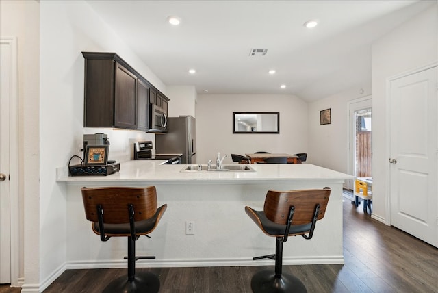 kitchen featuring sink, dark brown cabinets, kitchen peninsula, stainless steel appliances, and a breakfast bar area