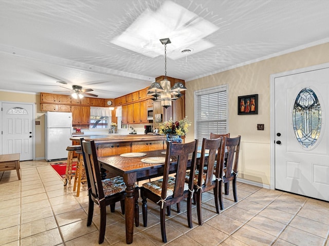 tiled dining space with ceiling fan with notable chandelier, a textured ceiling, and ornamental molding