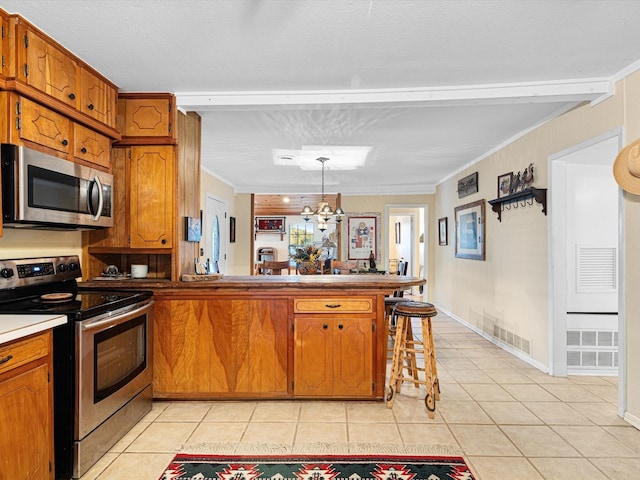 kitchen with kitchen peninsula, ornamental molding, stainless steel appliances, pendant lighting, and light tile patterned floors