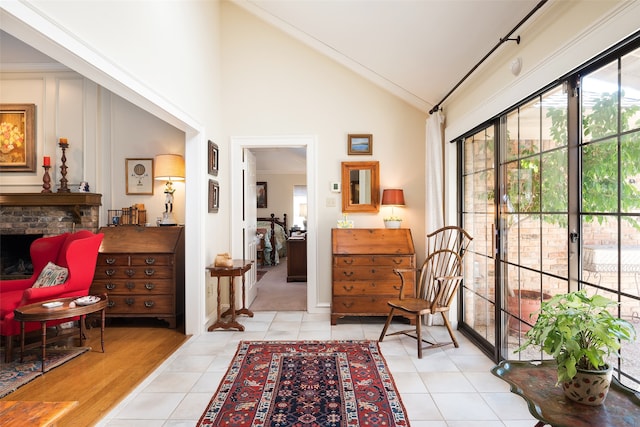 sitting room featuring high vaulted ceiling, ornamental molding, light tile patterned floors, and a brick fireplace