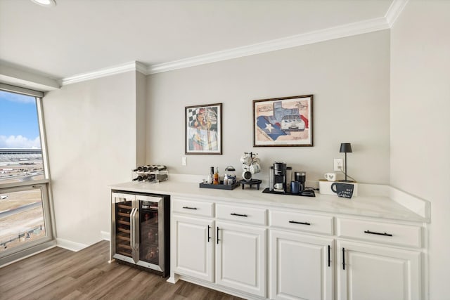 bar featuring wood-type flooring, ornamental molding, beverage cooler, white cabinets, and light stone counters