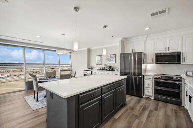 kitchen with hardwood / wood-style floors, white cabinetry, ornamental molding, pendant lighting, and stainless steel appliances