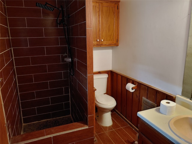 bathroom with toilet, wood walls, vanity, and tiled shower