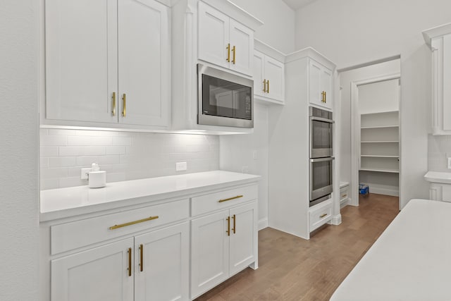 kitchen with decorative backsplash, white cabinets, stainless steel appliances, and hardwood / wood-style flooring