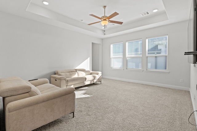 living room with a tray ceiling, carpet, and ceiling fan