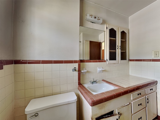 bathroom with toilet, vanity, and tile walls