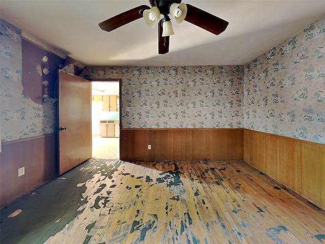 spare room with light hardwood / wood-style floors, wood walls, and ceiling fan