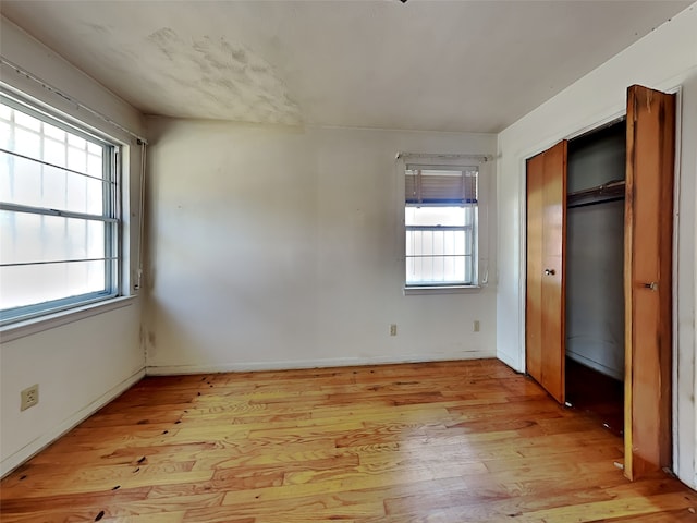 unfurnished bedroom with light hardwood / wood-style flooring, multiple windows, and a closet