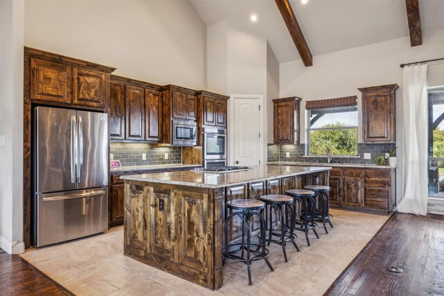 7817 Bella Flora Dr, Fort Worth, TX 76126 - kitchen featuring dark brown cabinetry, a kitchen island, a kitchen bar, light stone counters, and stainless steel appliances