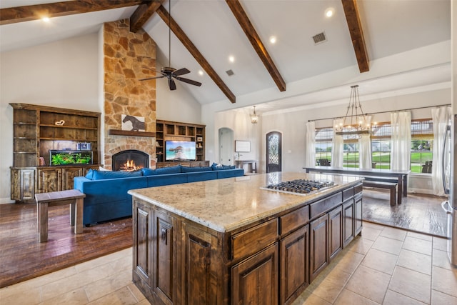 kitchen featuring a kitchen island, stainless steel gas stovetop, light hardwood / wood-style flooring, a stone fireplace, and decorative light fixtures